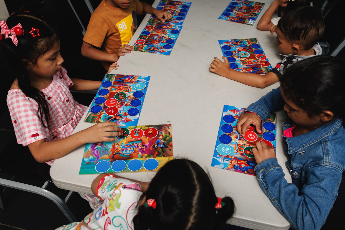 Niños trabajando con los tableros y las fichas de personajes sobre la mesa.
